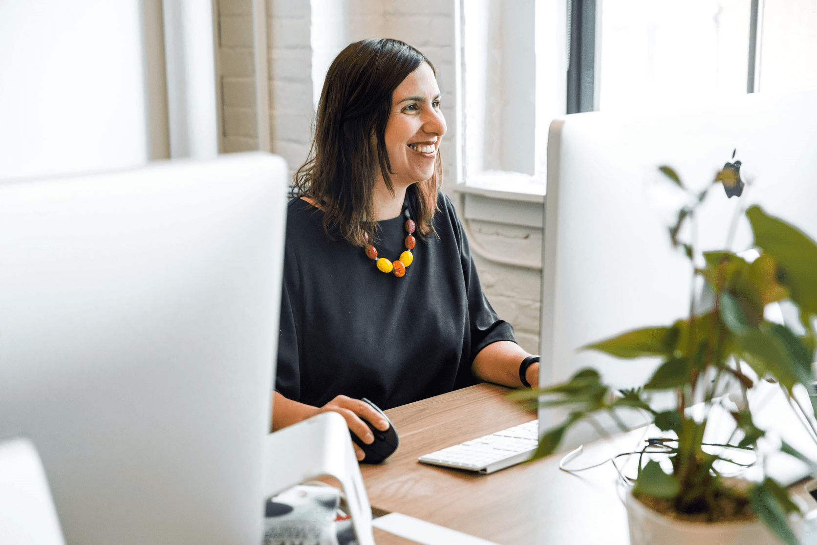 A woman smiles while focused on her computer screen, engaged in her work.