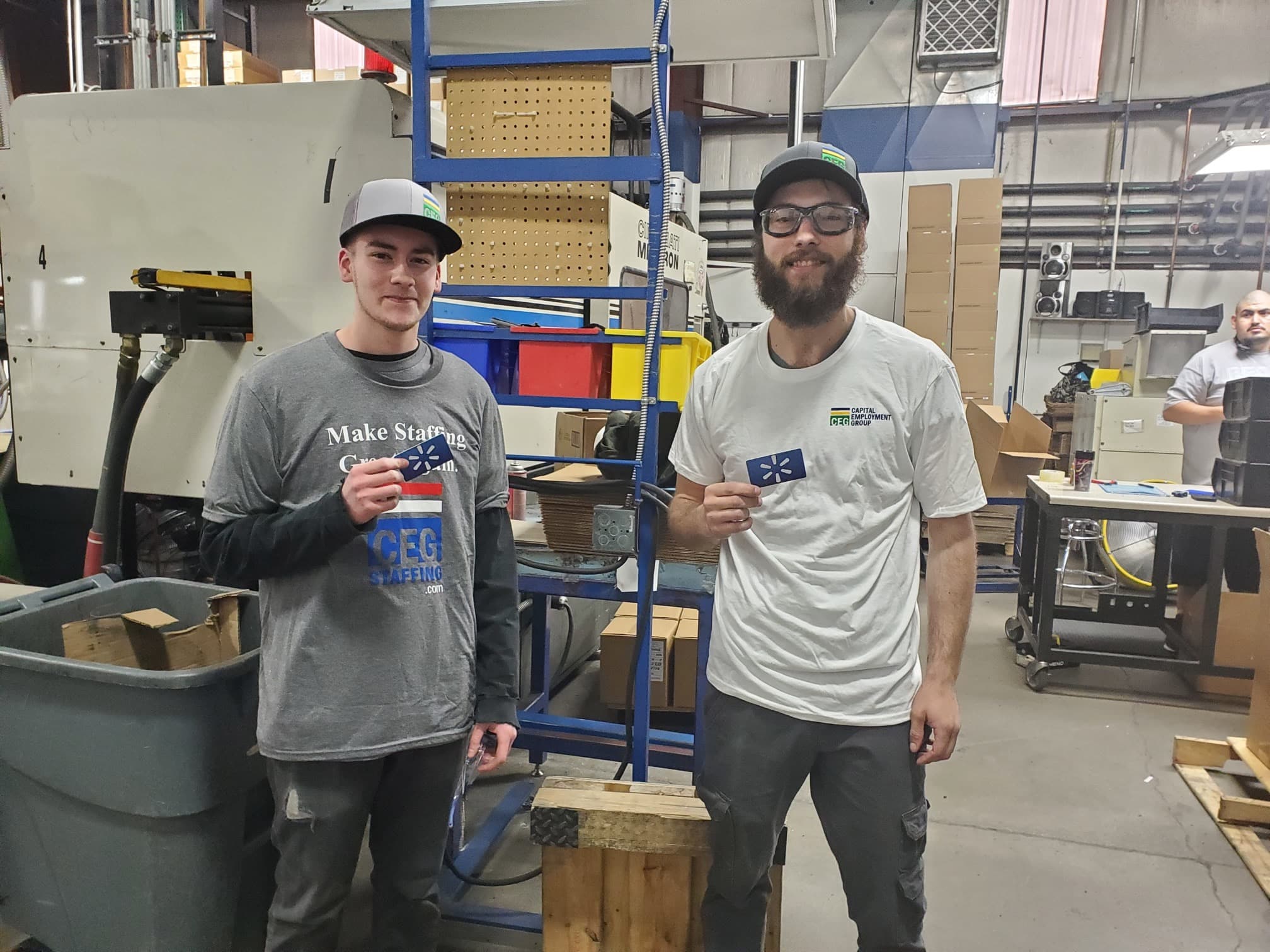Two men stand in front of a machine, each holding a card, engaged in a discussion about the device's operation.