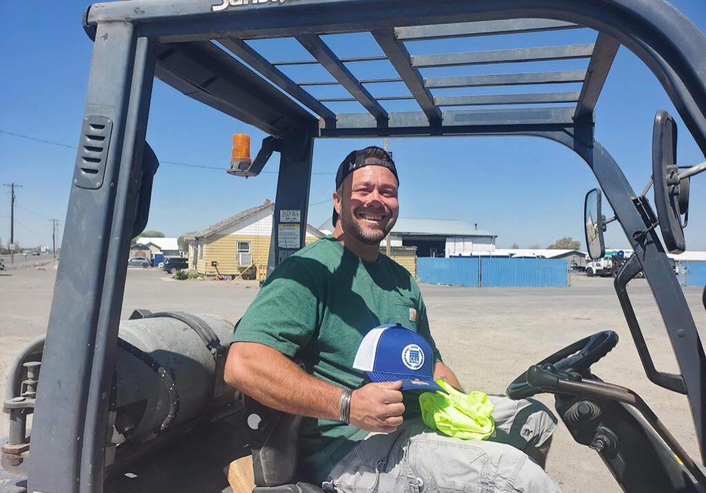 A man wearing a hat operates a forklift, focused on his task in a warehouse setting