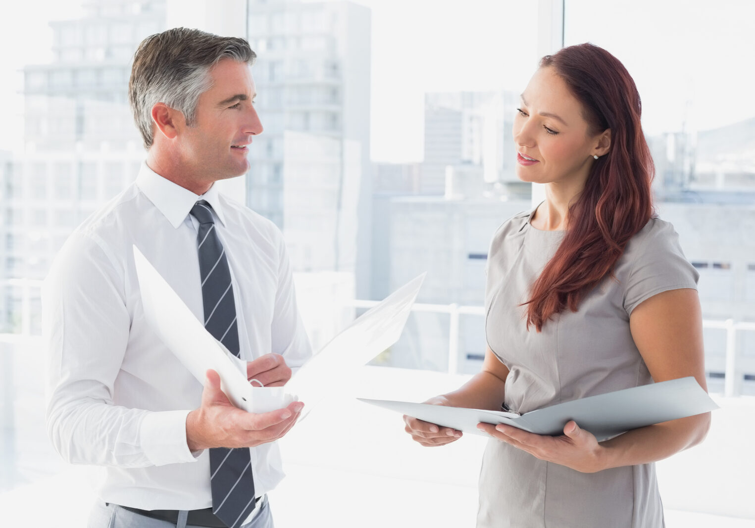 A man and woman in business attire engaged in a conversation, standing in a professional setting.