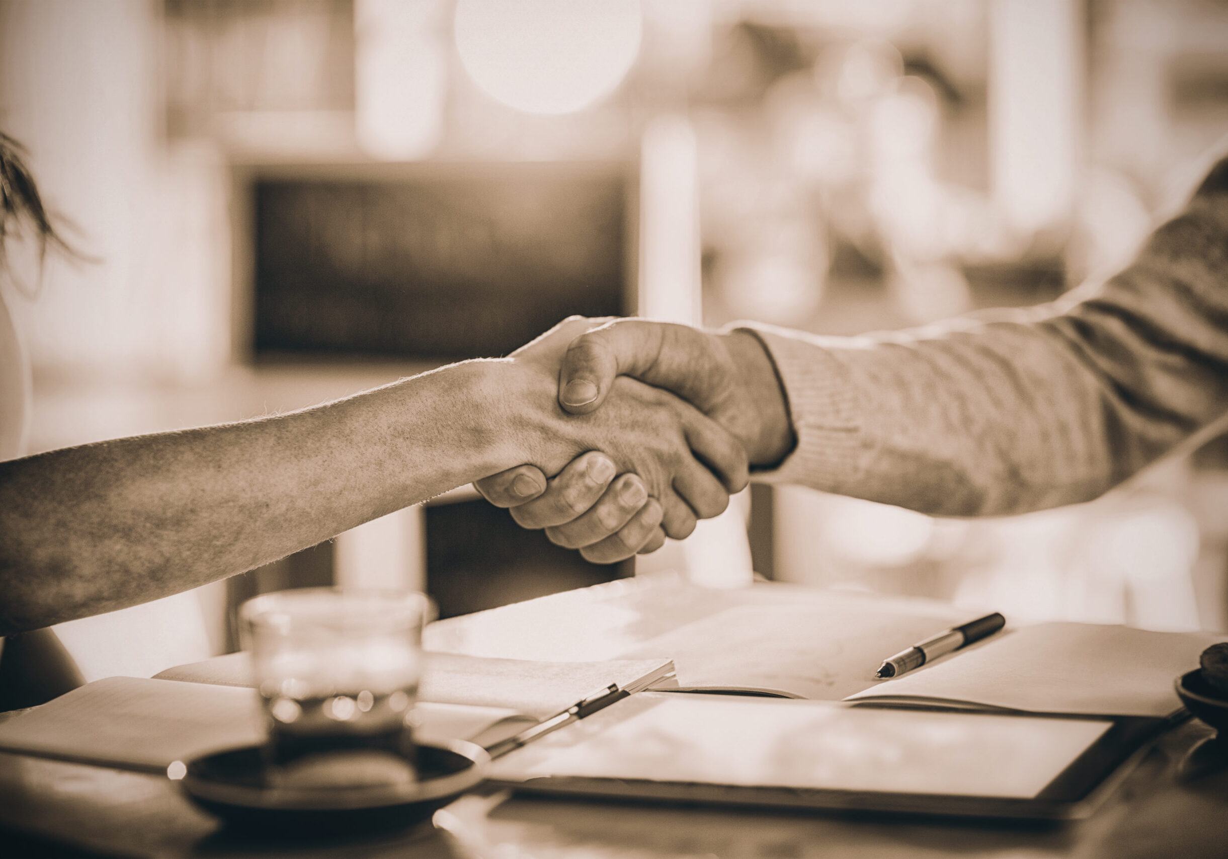 Two individuals shaking hands across a table, symbolizing agreement or partnership.